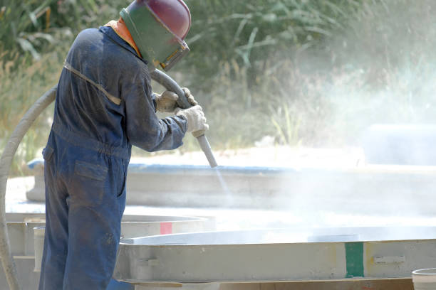 Worker is remove paint by air pressure soda blasting in a field